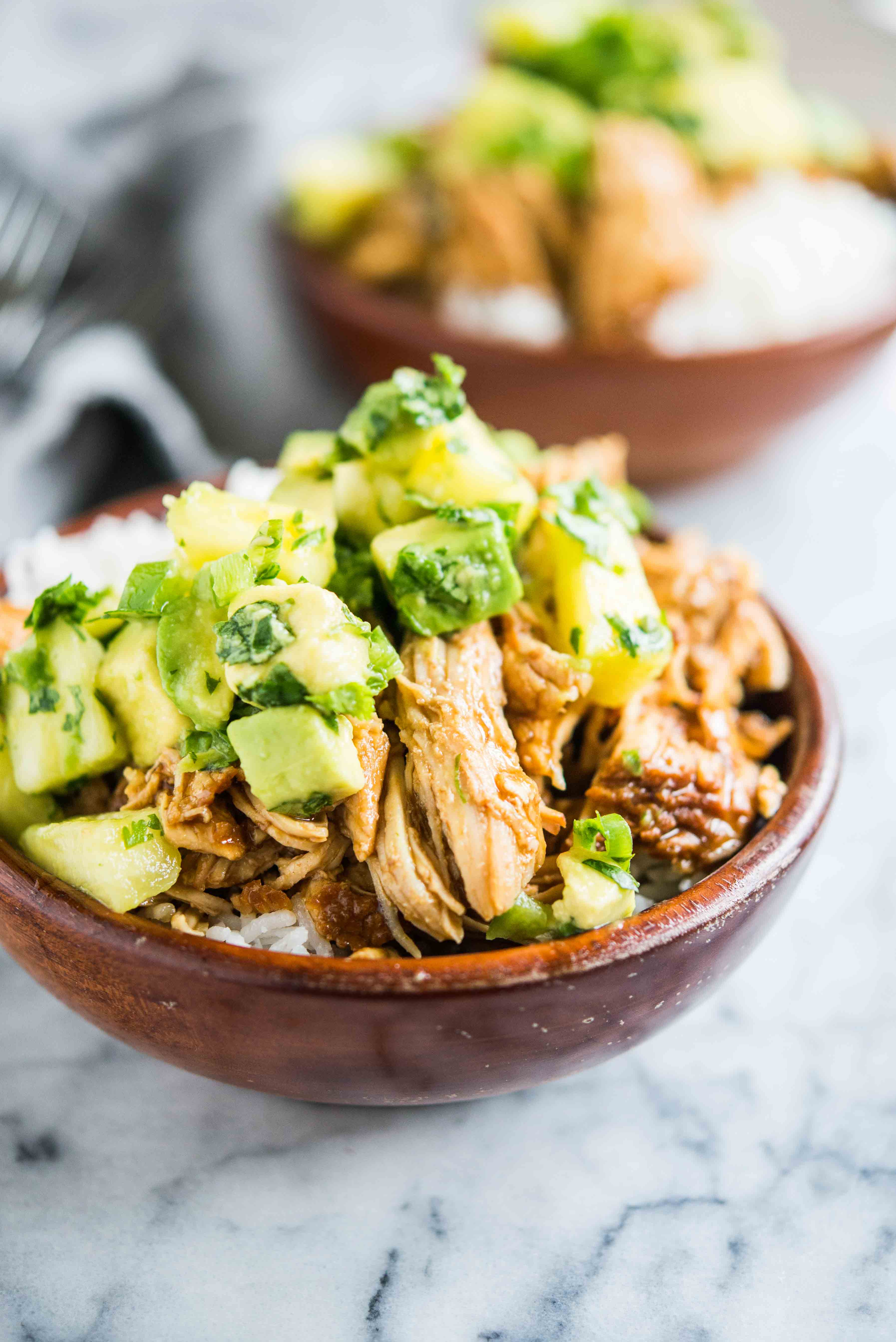 wooden bowls filled with white rice topped with island chicken and pineapple avocado salsa on a marble board