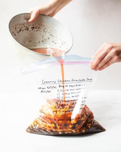 the ingredients for creamy enchilada soup being poured into a labeled freezer bag