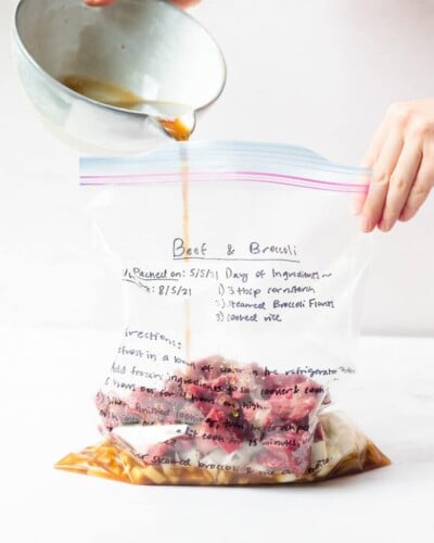 the ingredients for beef and broccoli being poured into a labeled freezer bag