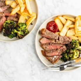 Two dinner plates with sliced steak, broccoli, and steak fries with a side of ketchup.