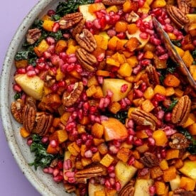 Harvest kale salad, in a grey bowl, sits on a purple background.